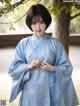 A woman in a blue kimono standing in front of a tree.