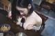 A woman sitting at a table with a bottle of beer.