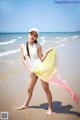 A woman standing on a beach holding a yellow and pink scarf.