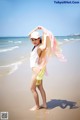 A woman standing on a beach holding a scarf.