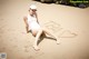 A woman in a white bathing suit sitting on a sandy beach.