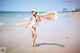 A woman in a white bathing suit and hat walking on the beach.