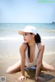 A woman in a white bathing suit and hat sitting on the beach.