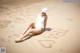 A woman in a white bathing suit sitting on a sandy beach.