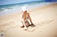 A woman sitting on the beach writing in the sand.