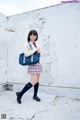 A woman in a school uniform holding a blue bag.