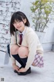 A young woman in a school uniform crouching down on the ground.