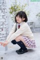 A young woman in a school uniform crouching on the ground.