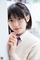 A young woman wearing glasses leaning against a wall.