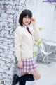 A woman in a school uniform leaning against a brick wall.