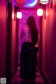 A woman standing in a hallway with pink lights.