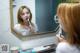 A woman brushing her teeth in front of a mirror.