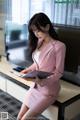 A woman in a pink suit sitting on a bench reading a book.