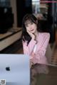 A woman in a pink suit sitting at a table with a laptop.