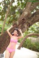 A woman in a pink bikini leaning against a tree.