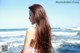 A woman with long brown hair standing on the beach.