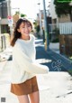 A woman in a white sweater and brown skirt posing for a magazine.