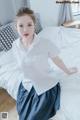 A woman in a white shirt and blue skirt posing on a bed.