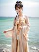 A woman in a kimono standing on a beach next to the ocean.