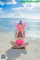 A woman in a bikini sitting on the beach holding a pair of flippers.