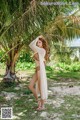 A woman in a bikini standing under a palm tree.