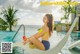 A woman in a yellow bikini sitting on a lounge chair by a pool.