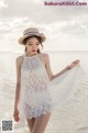 A woman in a white dress and hat standing on the beach.