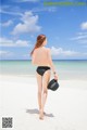 A woman in a black bikini walking on a beach.