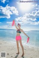 A woman standing on a beach holding a pair of flip flops.