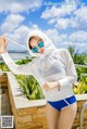 A woman in a white hoodie and blue shorts posing by a pool.