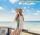 A woman in a bathing suit and hat sitting on a bench by the ocean.