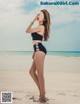 A woman in a black bikini standing on a beach.