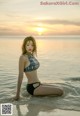 A woman in a bikini sitting in the water at sunset.