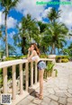 A woman in a bikini standing on a balcony next to palm trees.