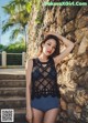 A woman in a black top and blue shorts leaning against a stone wall.