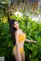 A woman in a yellow bikini posing in front of a palm tree.