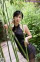 A woman in a black dress posing in front of a bamboo tree.