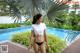 A woman in a white shirt and black bikini standing by a pool.