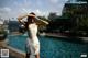 A woman in a white dress standing next to a swimming pool.