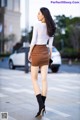 A woman in a white top and brown skirt is walking down the street.