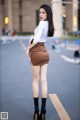 A woman in a white shirt and brown skirt is standing on the street.