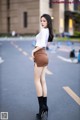 A woman in a white shirt and brown skirt standing in the middle of a street.