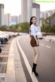 A woman in a white shirt and brown skirt standing on the side of a road.