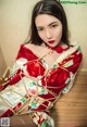 A woman in a red and white kimono sitting on a wooden floor.