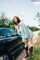 A woman standing next to a black car on the side of a road.