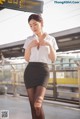 A woman in a white shirt and black skirt standing on a train platform.