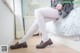 A woman sitting on a bed wearing white tights and brown shoes.