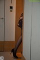 A woman in black stockings and high heels standing in a bathroom.