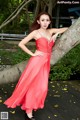 A woman in a red dress leaning against a tree.