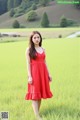 A woman in a red dress standing in a green field.